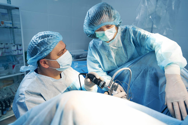 Male and female laparoscopic surgeons using tube camera during operation - Фото, изображение