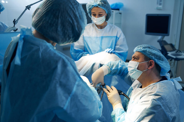 Surgeon with nurses doing operation with laparoscopic equipment - Foto, afbeelding