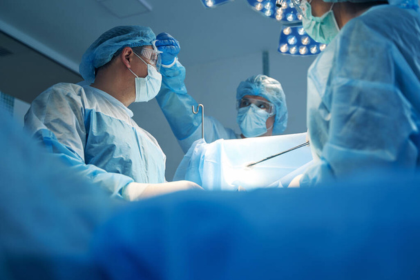 Νοσοκόμα σκουπίζοντας ιδρώτα από το μέτωπο χειρουργός κατά τη διάρκεια της επέμβασης - Φωτογραφία, εικόνα