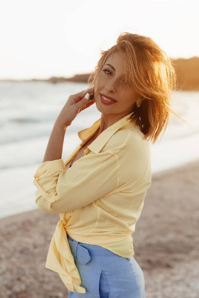 Happy mature woman feeling the breeze at beach. Beautiful middle aged woman on beach. Mid lady feeling good and enjoying freedom at sea, copy space. - Photo, Image