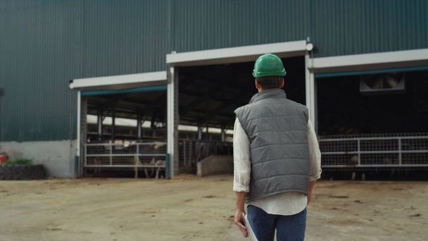 Maatilan kasvattaja kävelee moderni navetan takana näkymä. Maatalouden rakenteiden kehittäminen - Valokuva, kuva