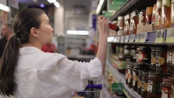 Μελαχρινή γυναίκα στα λευκά επιλέγοντας προϊόντα στα ράφια των σούπερ μάρκετ - Πλάνα, βίντεο