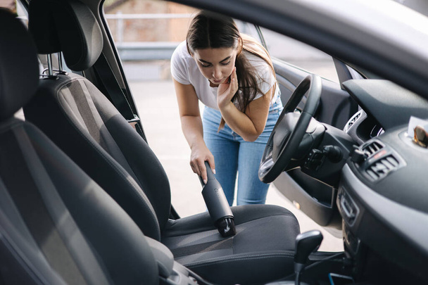 Woman vacuuming her car in the garage at home. Female using portable vacuum cleaner to remove dust and dirt. Car interior cleaning - Foto, Bild
