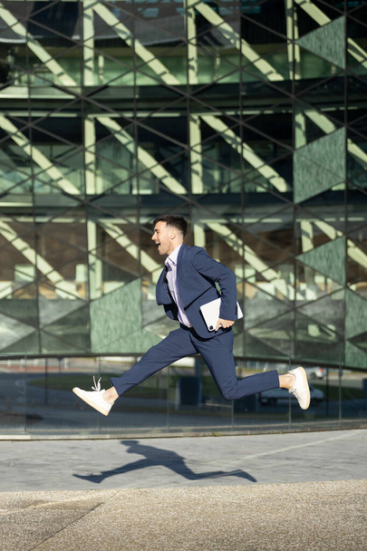 Молодий сучасний бізнесмен стрибає тримаючи планшет. Успіх бізнесу
 - Фото, зображення