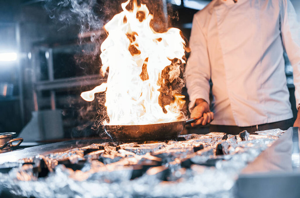Frying pan is on fire. Chef in white uniform cooking food at kitchen. Busy day at work. - Fotoğraf, Görsel