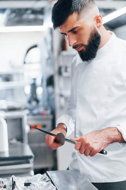 Chef in white uniform standing at kitchen. Holding knives in hands. - Foto, immagini
