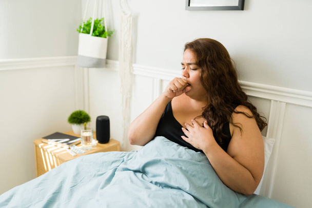 Ανθυγιεινή χοντρή γυναίκα με άσχημο κρύο βήχα και αδιαθεσία ενώ ξεκουράζεται στο δωμάτιό της - Φωτογραφία, εικόνα