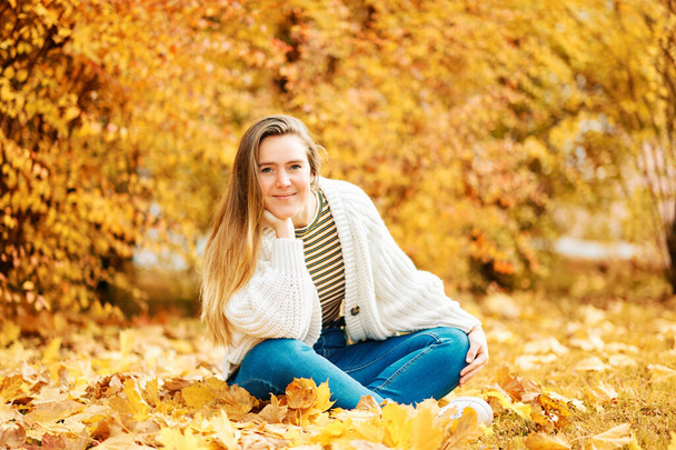 Autumn portrait of young happy girl sitting on ground with yellow foliage background, healthy lifestyle - Photo, Image