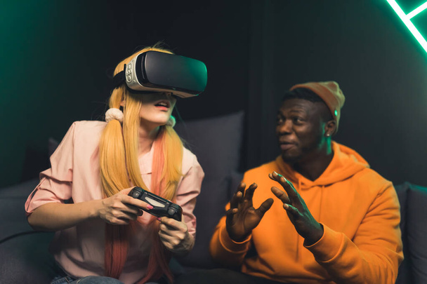 Blanke vrouw en Afro-Amerikaanse jonge man spelen videospelletjes met vr bril en joystick medium shot  - Foto, afbeelding