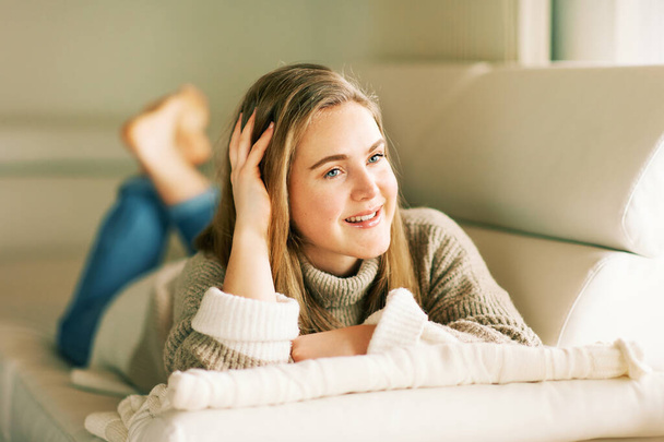 Ritratto indoor di giovane ragazza carina di 20 anni sdraiata sul divano, con indosso un pullover caldo - Foto, immagini