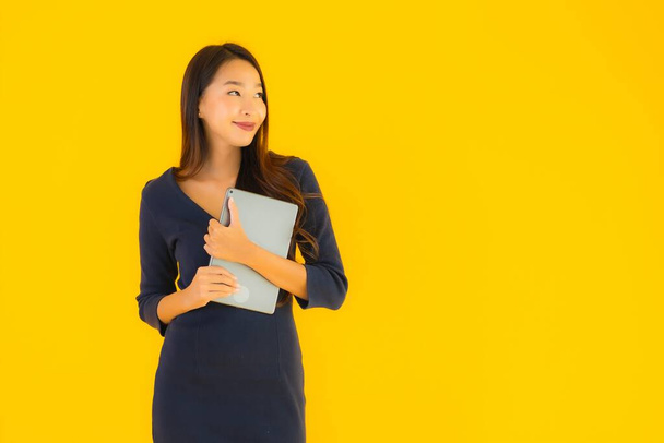 Retrato hermosa joven asiática mujer con inteligente tableta electrónica en amarillo aislado fondo
 - Foto, Imagen