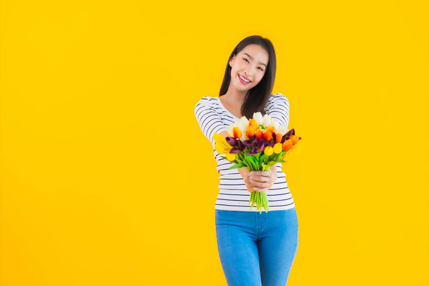 Portret mooie jonge aziatische vrouw met kleurrijke bloem op geel geïsoleerde achtergrond - Foto, afbeelding