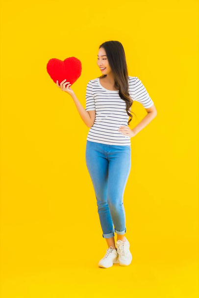 Portrait beautiful young asian woman show heart pillow on yellow isolated background - Foto, Imagen