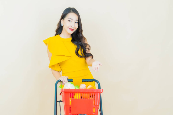 Porträt schöne junge asiatische Frau lächeln mit Einkaufskorb aus dem Supermarkt auf farbigem Hintergrund - Foto, Bild