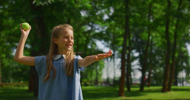 笑顔の女の子の緑の牧草地の閉鎖にボールを投げる。幸せな子供の遊びのキャッチで公園. - 写真・画像