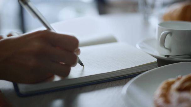 女性の手ノートを取るリモートワークプレイスカフェテーブルでペンノートを書く. - 写真・画像