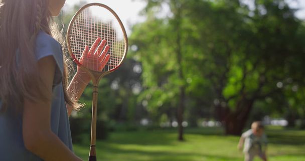 Ragazza annoiata giocare badminton con fratello toccando rete racchetta nel parco. Vista posteriore - Foto, immagini