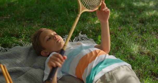 Aufgebrachter kleiner Junge liegt Decke im Park. Kind untersucht Badminton-Schlägernetz  - Foto, Bild