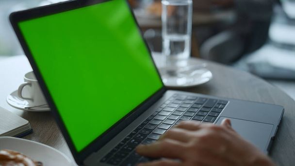 カフェレストランテーブルでキーボードのノートパソコンの緑の画面を入力する人の手. - 写真・画像