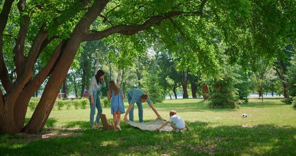 Mladý rodinný piknik na trávníku. Rodiče připravují oběd se dvěma dětmi. - Fotografie, Obrázek