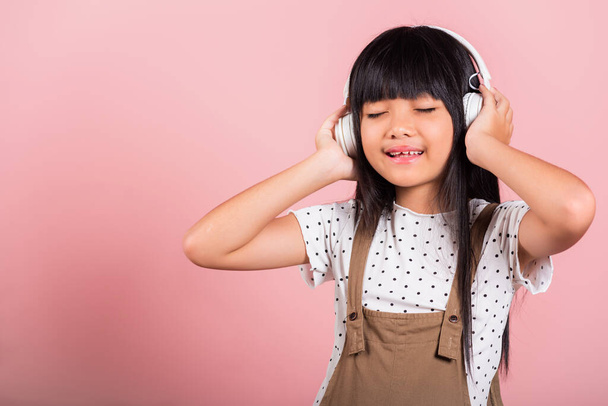 Asian little kid 10 years old smiling listening music wearing wireless headset at studio shot isolated on pink background, Happy child girl lifestyle listen music with headphones keeping eyes closed - Photo, image