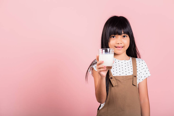 Asian little kid 10 years old smile hold milk glass drink white milk at studio shot isolated on pink background, Happy child girl daily life health care Medicine food - Fotoğraf, Görsel