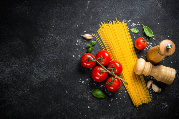 Italienisches Essen am schwarzen Tisch. Nudeln, Olivenöl, Gewürze, Basilikum und frische Tomaten. Draufsicht mit Kopierraum. - Foto, Bild