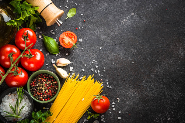 Italienische Lebensmittel Hintergrund auf schwarz. Nudeln, Olivenöl, Gewürze, Basilikum und frische Tomaten. Draufsicht mit Kopierraum. - Foto, Bild