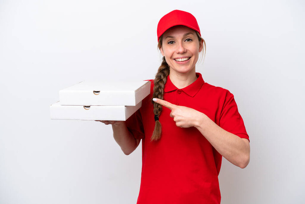 repartidor de pizza con uniforme de trabajo recogiendo cajas de pizza aisladas sobre fondo blanco apuntando hacia un lado para presentar un producto - Foto, Imagen