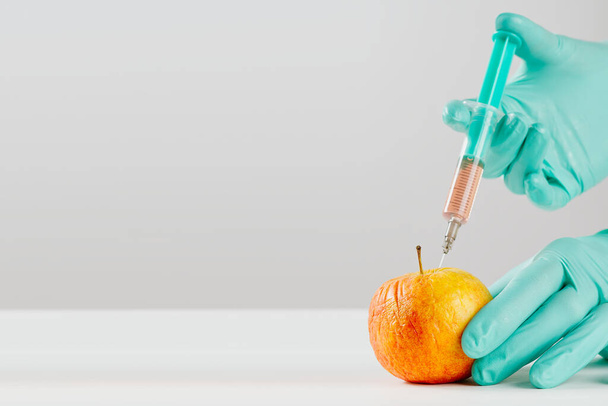A hand in a medical glove inserts a syringe into apple. Harmful food additives. GMOs Concept - Foto, Imagem