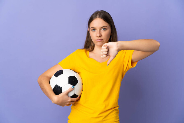 Молодая литовская футболистка, изолированная на фиолетовом фоне, показывает большой палец вниз с негативным выражением - Фото, изображение