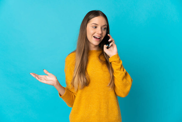 Young Lithuanian woman isolated on blue background keeping a conversation with the mobile phone with someone - Φωτογραφία, εικόνα
