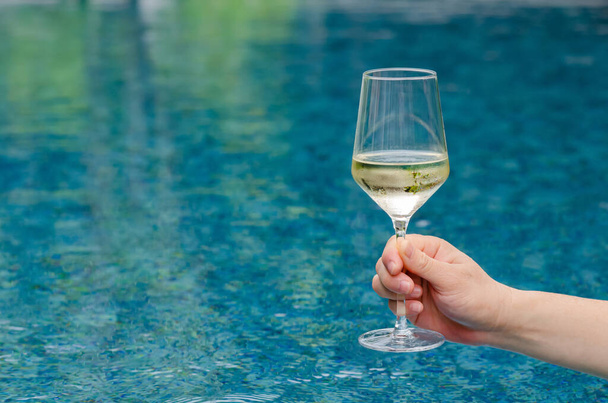 Tenendo in mano un bicchiere di vino bianco con fondo piscina. Vacanza e concetto di bevanda estiva. - Foto, immagini