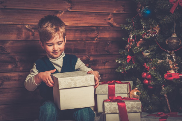 Petit garçon avec boîte cadeau sous l'arbre de Noël à l'intérieur de la maison en bois
  - Photo, image