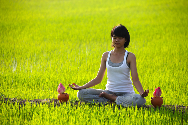 Mädchen praktiziert Yoga, sitzt mit Lotusblume im Reisfeld - Foto, Bild