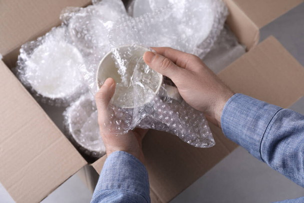 Man covering ceramic dishware with bubble wrap, closeup - Foto, afbeelding