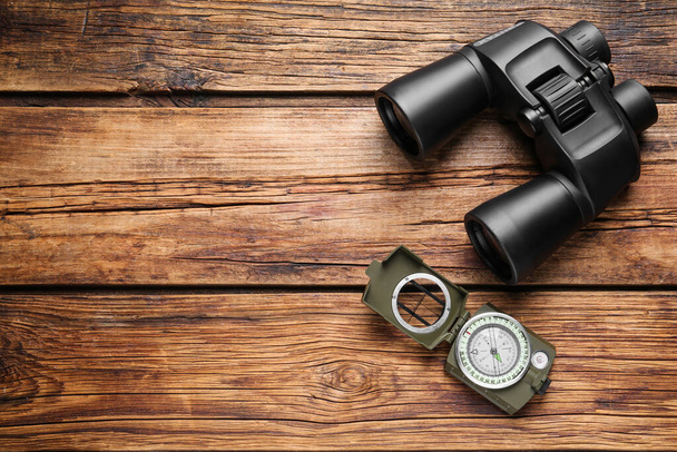 Binoculars and compass on wooden table, flat lay. Space for text - Фото, зображення