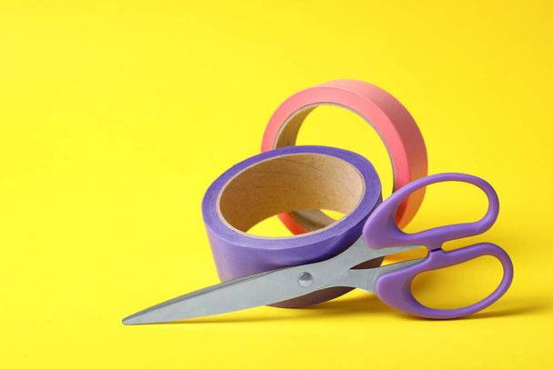 Two rolls of adhesive tape and scissors on yellow background. Space for text - Φωτογραφία, εικόνα