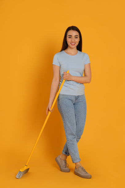 Beautiful young woman with broom on yellow background - Photo, Image