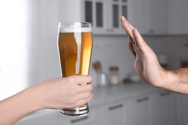 Man refusing to drink beer in kitchen, closeup. Alcohol addiction treatment - Фото, зображення