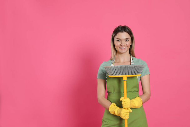 Young woman with yellow broom on pink background, space for text - Foto, Imagen