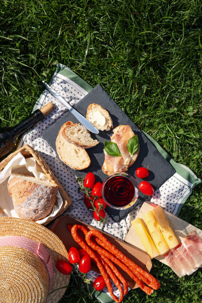 Blanket with wine and snacks for picnic on green grass, flat lay - Φωτογραφία, εικόνα