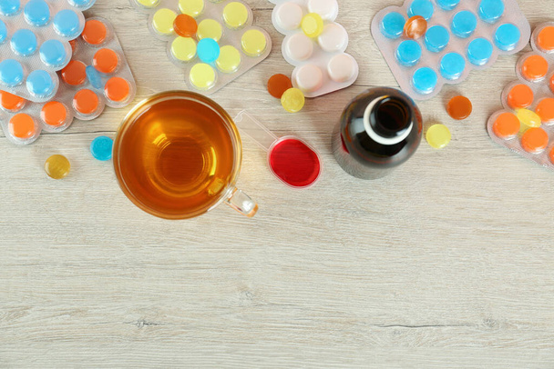 Flat lay composition with cough syrup, lozenges and cup of tea on white wooden table, space for text - Fotografie, Obrázek