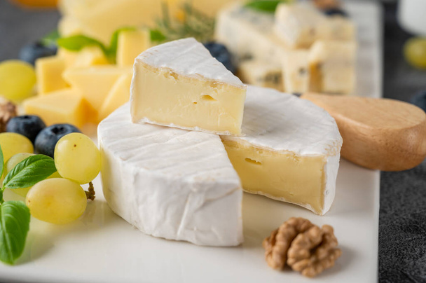 Sýrový talíř s různými sýry, medem, hrozny, ořechy, olivami, borůvkami a čerstvými bylinkami na betonovém podkladu. Slavnostní svačinka - Fotografie, Obrázek
