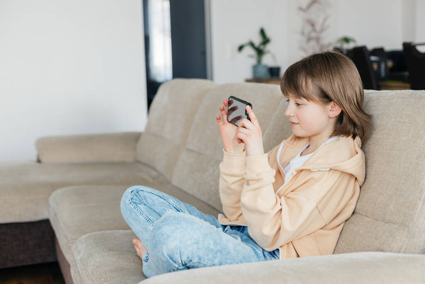Школярка сидить на дивані і грає на мобільному телефоні або спілкується з друзями. Діти використовують технології. Сучасні гаджети та підлітки
. - Фото, зображення