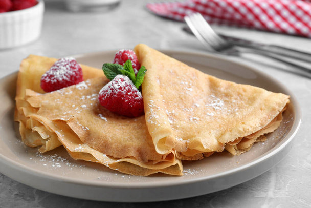 Delicious crepes served with mint, raspberries and powdered sugar on grey table, closeup - Foto, immagini
