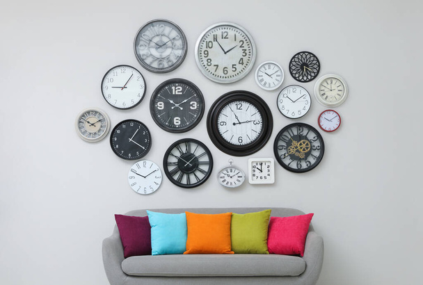 Sofa and many different clocks hanging on white wall in room - Valokuva, kuva
