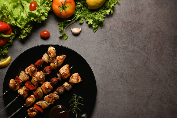 Delicious barbecue skewers with grilled chicken, cherry tomato, sweet pepper, onions and barbecue sauce on dark stone background - Photo, Image