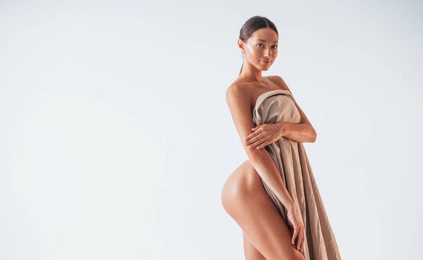 Standing and covering body by cloth. Beautiful woman is in the studio. - Foto, Bild