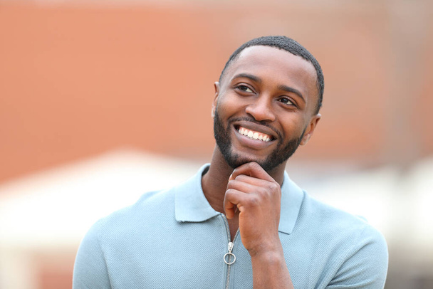 Front view portrait of a happy man with black skin thinking looking at side in the street - Photo, Image